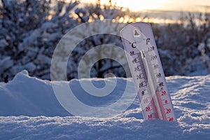 Thermometer on snow shows low temperatures in celsius or farenheit. On the Sunset photo