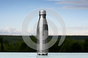 Thermos bottle sprayed with water. Against the sky background. Water tumbler.