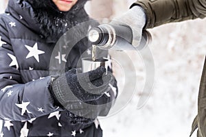 Thermos and cold season concept - A woman pours a hot drink. Couple on a winter holiday