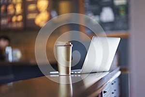 Thermos cup & laptop on table inside a coffee shop