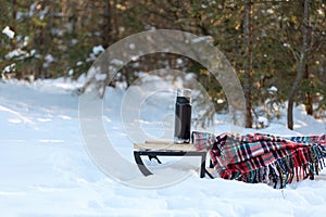 Thermos on sleigh in winter snowy forest and checkered plaid. Picnic in winter time. Nobody. Snowy day