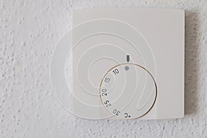 Thermostat with the external and target temperatures indicated. Rotary dial to control and adjust. White wall and white