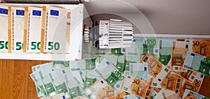 Thermostat of the heating radiator battery, in the background there are many banknotes of 50 and 100 euros