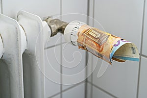 Thermostat on an old radiator wrapped with euro banknotes, concept for rising cost of heat and energy in a cold winter, selected