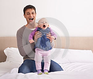 Theyre having so much fun together. A young father playing with his baby girl on the bed.