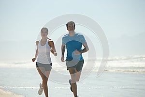 Theyre in it for the long run. a young couple jogging together on the beach.