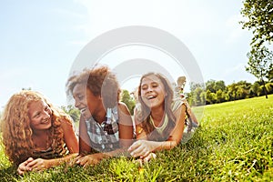 Theyve got all the jokes to tell. three young girls lying together on the grass outside.