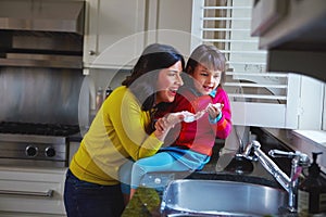 Theyve got no trouble with bubbles. a young mother and her daughter playing by the kitchen sink.