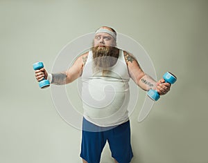 Thick bearded guy lifting dumbbells with effort