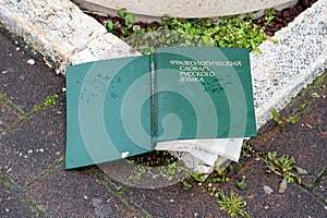 A thick book in hardcover lies on the street, thrown away on the cover is written in Russian - Phraseological Dictionary of the photo