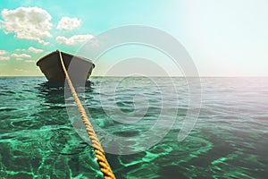 A thick clothesline is tied to an anchor that lies at the bottom of a clear blue sea, keeping the green boat on the surface in