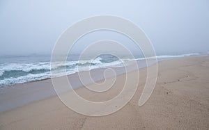 Thick, dense fog over the ocean as waves break on the empty beach.