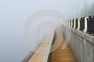 Thick fog on the city embankment. Yellow sand deposits on the lower level after the flood.