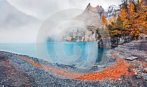 Thick fog gloving mountain peaks and lake. Calm autumn view of unique Oeschinensee Lake. Misty morning scene of Swiss Alps with Bl