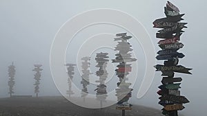 Thick fog and strong wind on mount Mashuk. Famous observation deck with distance signs to different cities of the world.