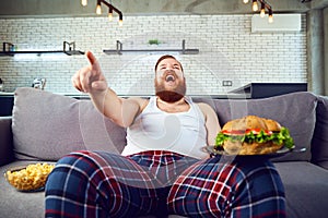 Thick funny man with a burger sitting on the couch.