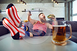 Thick funny man eating a burger sitting on the couch.