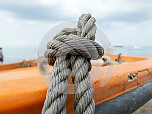 Thick grey rope tied to small orange boat photo
