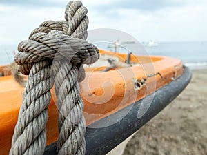 Thick grey rope tied to small orange boat photo