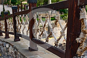 Thick rope ropes, intertwined crosswise, hang on wooden railings, decorative fence along the alley in the Park for recreation.