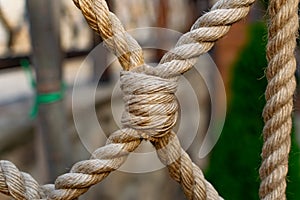 Thick rope ropes, intertwined crosswise, hang on wooden railings, decorative fence along the alley in the Park for recreation.