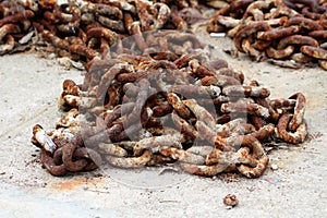 Thick strong rusted metal chain removed from ship anchor and left on concrete pier after being replaced with new and improved