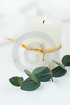Thick White Lit Candle with Twine and Dry Plant Twig Silver Dollar Eucalyptus White Cloth Background Copy Space