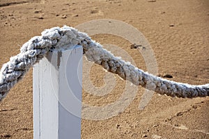 A thick white rope in a bow shape hangs on wooden poles on brown sea sand