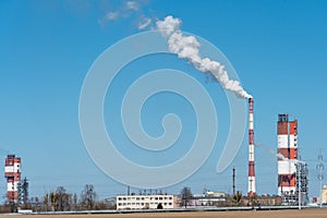 Thick white smoke coming out of a large pipe of an industrial facility or factory. A smoking chimney against a blue sky.