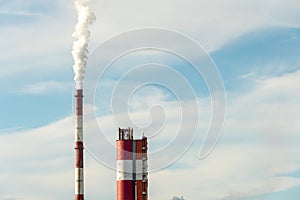 Thick white smoke coming out of a large pipe of an industrial facility or factory. A smoking chimney against a blue sky.