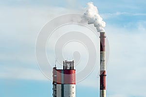 Thick white smoke coming out of a large pipe of an industrial facility or factory. A smoking chimney against a blue sky.