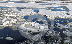 Thick white snow-covered ice floes float along a wide river