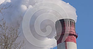 Thick white steam escapes from the chimney of the thermal power plant and dissipates into the blue sky.