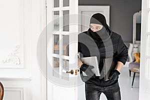 Thief with black balaclava stealing two modern expensive laptops. The burglar commits a crime in Luxury apartment with