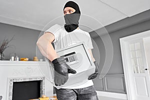 Thief with black mask stealing modern Metal safe with an electronic lock. Home theft of money and documents concept.