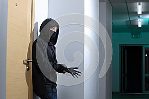Thief broke into the apartment. House robbery by woman in a black jacket and black mask black gun and crowbar. Burglar in a mask.