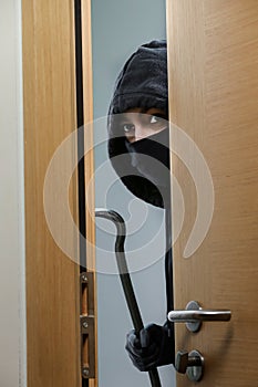 Thief broke into the apartment. House robbery by woman in a black jacket and black mask black gun and crowbar. Burglar in a mask.