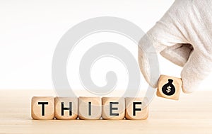 Thief concept. Hand picking a wooden block whit money bag icon and text on wooden dice