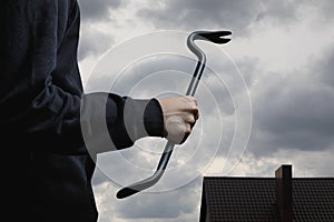 A thief with a crowbar in front of a sky and the roof of a house