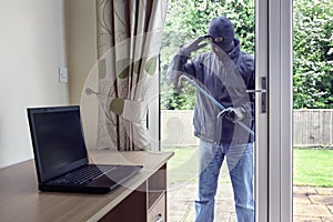 Thief looking through patio doors window at a laptop computer to