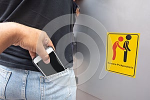 Thief stealing mobile phone from back pocket of a woman with beware pickpockets sign symbol background.