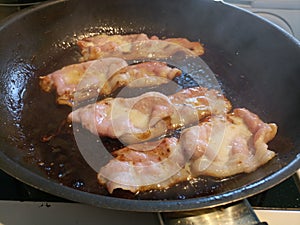 Thin bacon rasher sizzling in a oily pan