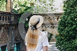 A thin blonde girl with long hair in a white dress stands with her back to the camera and looks into the distance in a wide-