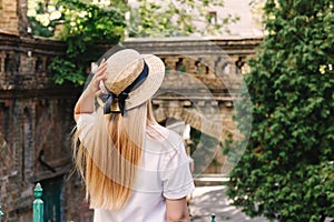 A thin blonde girl with long hair in a white dress stands with her back to the camera and looks into the distance in a wide-