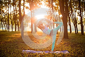 Thin brunette girl doing Natarajasana exercise, Lord of the Dance pose in autumn park on a sunset background. Woman doing