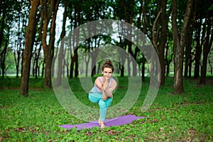 Thin brunette girl plays sports and performs beautiful and sophisticated yoga poses in a summer park. Green lush forest on the