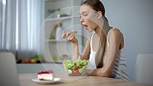 Thin female eating vegetable salad but dreaming about tasty cake, temptation