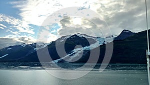 Thin Glacier between two mountains slowly gliding into the pacific ocean with a cloudy backdrop