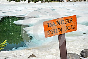 Thin ice warning notice on orange danger signboard by mountain lake
