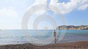 Thin man in bathing shorts trying water before diving into endless Aegean Sea